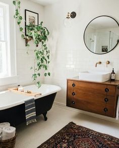 a bath tub sitting next to a sink in a bathroom under a mirror and potted plant