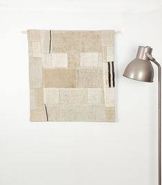 a lamp is next to a white wall with a patchwork design on it and a rug hanging from the side