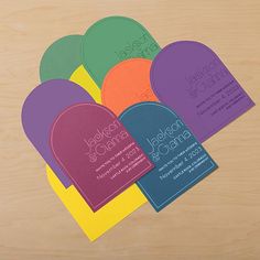 four business cards sitting on top of a wooden table next to an orange, green, purple and yellow envelope