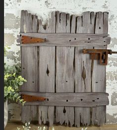 an old wooden door with rusted metal latches on the side and flowers in vase next to it