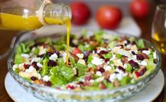 someone pouring dressing onto a salad in a bowl