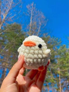 a hand holding a small white sheep toy in front of some trees and blue sky