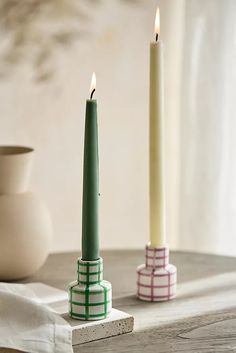 two candles sitting on top of a wooden table next to a white vase with a green candle in it