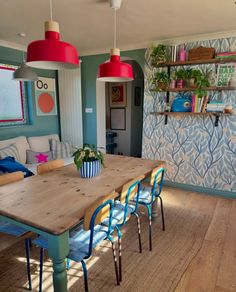 a dining room table with blue chairs next to a couch and shelves on the wall