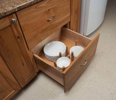 an open drawer in the middle of a kitchen with plates and bowls on it's side