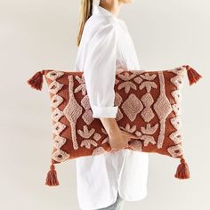 a woman is holding a decorative pillow with tassels on the back and sides