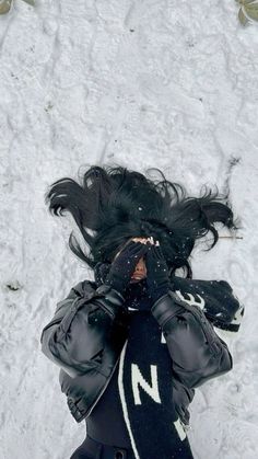 a woman laying in the snow with her hands on her face and hair blowing back