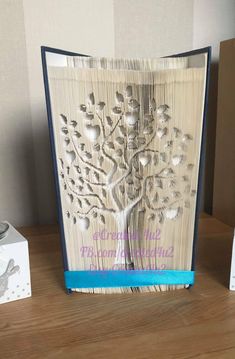 an open book with a tree cut out of it on top of a wooden table