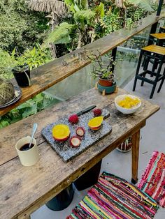 an outdoor table with bowls of fruit on it, and two cups of coffee sitting next to each other