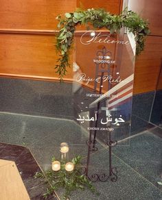 a glass sign with candles and greenery on it in front of a wooden wall