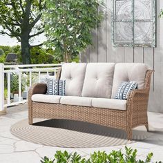 a wicker couch sitting on top of a patio next to a wooden fence and trees