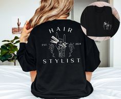 "This personalized \"Hair Stylist EST. 2024\" sweatshirt would make the perfect graduation gift for new hairstylists! Want this in a t-shirt instead? You can find it here: https://www.etsy.com/listing/1647306488 *HOW TO ORDER* 1. Look through photos at the different colors and the sizing chart (all shirts & sweatshirts are unisex!) 2. Select your size and color from the drop down menus. 3. Choose the quantity you want in that size and color. 4. If applicable, add your custom wording under the \"personalization\" tab. 5. Click \"add to cart\" then you can go back and add different colors and sizes the same way if wanted. 6. Click \"proceed to check out\" 7. Wait for your new favorite shirt to come in and enjoy!   *SHIRT MATERIALS* - 100% combed and ring-spun cotton (Heather colors contain p Cosmetologist Shirt Ideas, Cosmetology Graduation Gifts, Hairstylist Shirt Ideas, Hairstylist Outfits For Work, Salon Merch, Hairdresser Outfit, Hairdresser Outfit Work, Hairstylist Tshirts, Salon Shirts