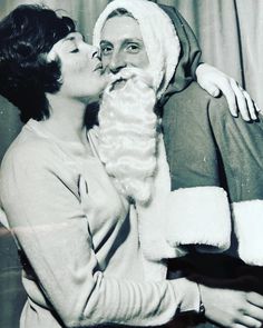 an old black and white photo of a man kissing a woman in front of a christmas tree