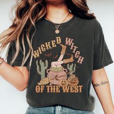 Stir up some Halloween fun with our "Wicked Witch of the West" T-shirt! This enchanting design features a bubbling cauldron with legs in cowgirl boots sticking out, surrounded by whimsical decorations like cacti, a broomstick, and jack-o-lanterns. Perfect for adding a touch of spooky Western charm to your fall wardrobe, this shirt is ideal for Halloween parties, casual outings, or cozying up with a spellbook. Made from soft, high-quality fabric, it ensures comfort and style as you embrace your w Witchy Halloween T-shirt With Letter Print, Halloween Cartoon Print Relaxed Fit Tops, Witchy Graphic Print Crew Neck Tops, Witchy Letter Print T-shirt For Fall, Witchy Cotton Crew Neck Tops, Witchy Cotton Tops With Letter Print, Witchy Short Sleeve T-shirt With Graphic Print, Witchy Halloween Crew Neck T-shirt, Witchy Halloween T-shirt With Graphic Print