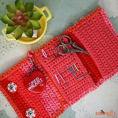 there is a red crochet bag with scissors and a heart on it next to a potted plant