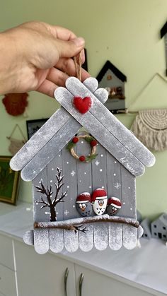 a person is holding up a birdhouse ornament with two birds on it