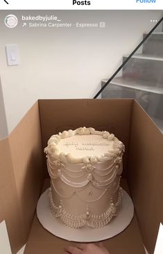 a cake in a box being held up by someone's hand, with stairs in the background