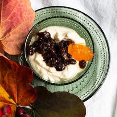 a bowl filled with cream and fruit on top of a green plate next to leaves