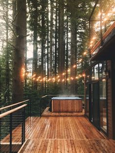 a wooden deck with hot tub surrounded by trees and string lights hanging from the ceiling