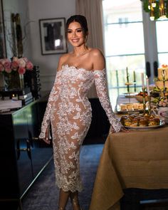 a woman standing in front of a table with food and drinks on it, wearing an off the shoulder dress