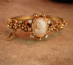 "This victorian style vintage bracelet holds a genuine cameo. Signed Florenza. Ornate raised baroque flowers surround the beautiful center piece genuine cameo on this stunning and charming hinged bangle bracelet. The stones are around it are faux moonstones which give it quite an eerie effect. The bracelet measures 7\" long on the inside and it has its original safety chain. The back of the band has ornate fancy etchings. The hinge and clasp work well. Inside it is marked Florenza. 2-2-19" Elegant Bangle With Antique Finish, Elegant Antique Finish Bangle, Elegant Antique Finish Bangle Bracelet, Oval Cabochon Wedding Bracelet, Elegant Bangle Bracelet With Antique Finish, Oval Cabochon Bracelet For Wedding, Elegant Bangle Jewelry With Antique Finish, Elegant Formal Bracelet With Antique Finish, Elegant Antique Finish Formal Bracelets