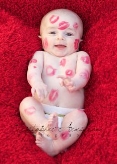 a baby with pink and red paint on it's body sitting on a red blanket