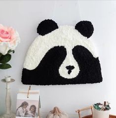 a black and white panda bear hat hanging on the wall next to a vase with flowers