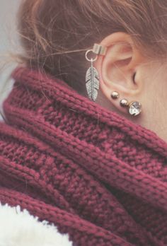 a close up of a person wearing ear rings and a sweater with leaves on it