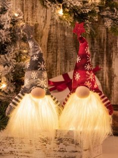 two christmas gnomes sitting next to each other in front of a tree with lights