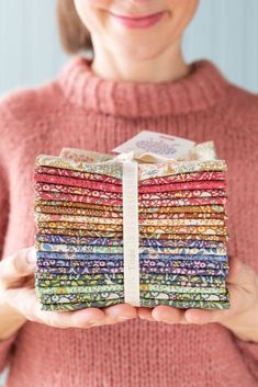 a woman holding a stack of multicolored cloths in her hands and smiling at the camera