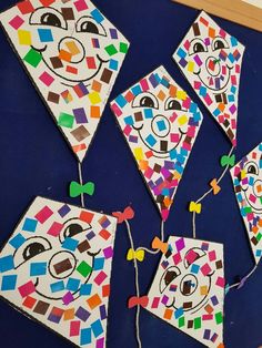 some colorful kites are hanging on a blue wall with string attached to them and one has a clown face painted on it