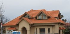 a tan house with orange roof tiles and a fence in front of it, on a cloudy day