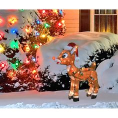 a lighted reindeer in front of a house with christmas lights on it's trees