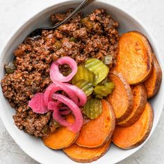 a bowl filled with meat and vegetables on top of a white countertop next to sliced onions