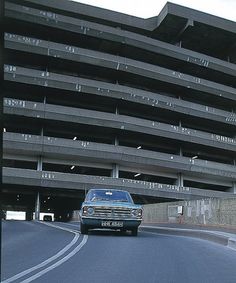 a car driving down the road in front of a large building with balconies