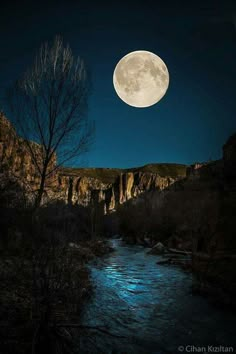 the moon shines brightly in the sky over a river and mountains with trees on either side