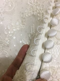 someone is stitching the lace on a white dress with buttons and sequins