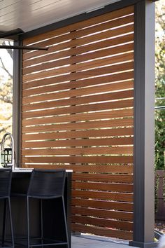 an outdoor kitchen with bar stools and wooden slatted screens on the wall