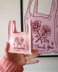 a hand holding a pink plastic bag with roses on it and the words thank you