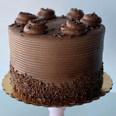 a chocolate cake with frosting and sprinkles sitting on a wooden stand