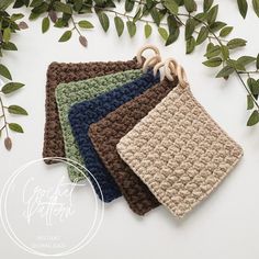 four crocheted potholders are hanging on a branch with green leaves in the background