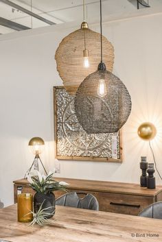 two lamps hanging from the ceiling above a wooden table with chairs and plants on it