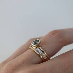 a woman's hand with two gold rings and an aqua blue diamond ring on it