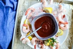 a plate with shrimp, lemons and ketchup on it next to a bowl of sauce