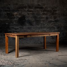 a wooden table sitting on top of a cement floor next to a brick wall with no one around it