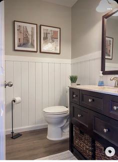 a white toilet sitting in a bathroom next to a wooden sink vanity with two framed pictures on the wall