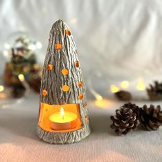 a lit candle sits next to some pine cones