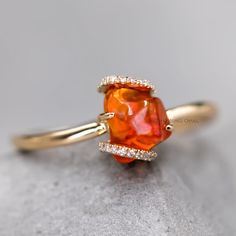 an orange and white diamond ring on top of a gray surface with gold trimmings