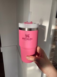 a person holding a pink tumbler cup in front of a white door with the word stanley on it