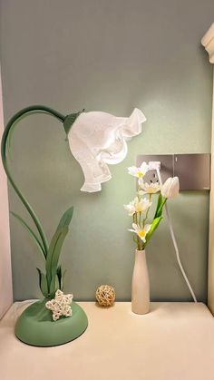 a white vase with flowers in it sitting on a table next to a light bulb